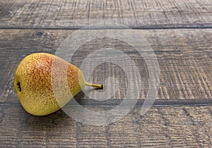 A ripe yellow pear with a pink side lies on a brown plank surface.