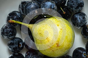 ripe yellow pear and plums in water on the table at home, one pear