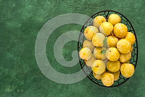 Ripe yellow plums in a metal basket on green background. Top view with copy space