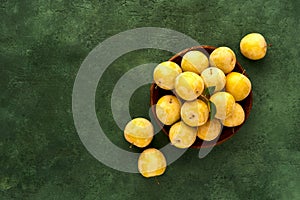 Ripe yellow plums in a wooden plate on green background. Top view with copy space