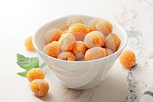 Ripe yellow raspberries in a bowl with a tea towel on a marble background. A bowl full of raspberries.