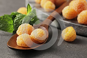 Ripe yellow raspberries in a wooden spoon on a marble background.