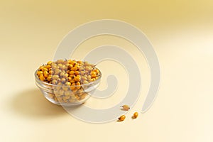 Ripe yellow sea buckthorn berries in a glass bowl on a yellow background.