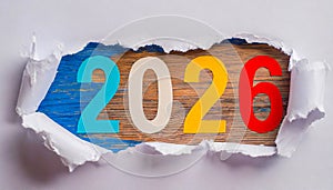 Ripped brown paper revealling the year 2026 written in colorful numbers on a white orange background.