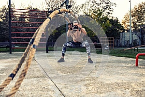 Ripped guy wearing a fitness mask doing cardio with battle ropes outside