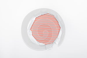 Ripped hole in textured white paper on red striped background.