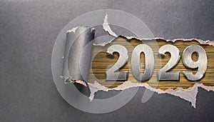 Ripped metallic paper revealling the year 2029 written in metallic numbers on wooden background