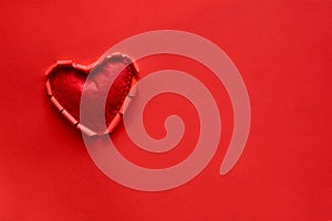 Ripped paper hole heart shaped with felt heart on red paper background. Valentine`s day celebration concept photo