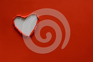 Ripped paper hole heart shaped on red paper background. Valentine`s day celebration concept