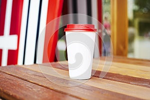 Ripple white paper cup to takeaway on wooden floor outside the cafe. Surfing boards stand behind at the background.
