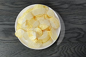 Rippled potato chips in white plate on wood table