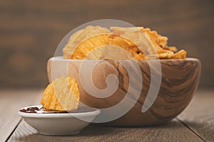 Rippled potato chips in wood bowl with sauce