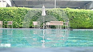 Rippled water in swimming pool with comfortable deck chairs and green plant background
