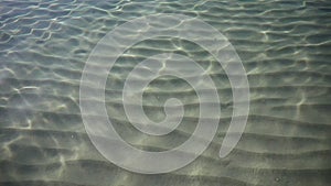 Ripples on surface of sand sea bottom, clear and calm blue sea water, fishes in water, nature texture