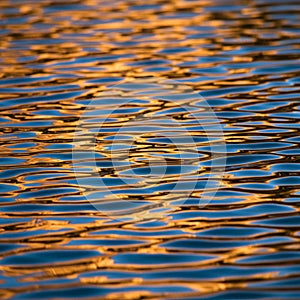 Rippling water surface reflecting golden sunlight, creating an abstract pattern of