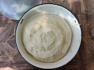 Risen or Proved Yeast Dough top view on the plate on the wooden background outdoor with sun glare.