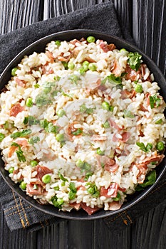 Risi e Bisi classic Italian comfort food of rice with peas and chunks of ham close up in a plate. Vertical top view