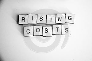 Rising Costs text on vintage wooden squares. Background concept for rising prices â€“ houses, bills, fuel, shopping. Soft blue