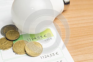 Rising energy costs concept: light bulb resting on an energy bill with some euro coins