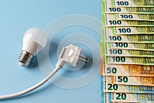 Rising energy prices. White electrical plug and light bulb at euro money banknotes over blue background. European power prices,