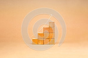 Rising up thin arrow on wooden cube blocks, bar graph chart steps on brown recycle paper background, profit, benefit, income,