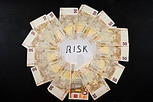 RISK inscription written in black marker on white and Euro banknotes on a black background. View from above. Business concept.