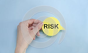 Risk text on yellow paper in hand on blue table - business, banking, finance and investment concept