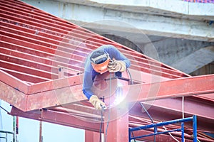 Risky welder while climbing and welding on top of the steel roof structure work at the building construction site. Skilled worker