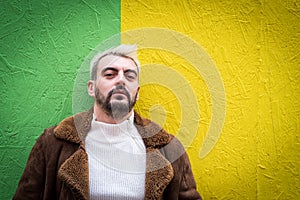 Portrait of a hipster with platinum blond hair and dark beard, wearing a white sweater and a brown coat, green and intense yellow photo