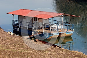 River barge converted into river boat house with improvised roof and terrace with white plastic chairs and tables