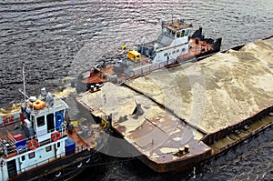 River barge loaded with sand. Close-up view of cargo ship barge loaded with sand. Top view of the of the barge with two tugboats