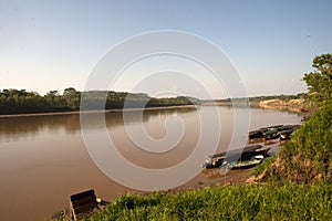 River Boats tied up to pier along muddy and grassy river bank with view to other shore in Puerto Maldonado in Peru and the Amazon