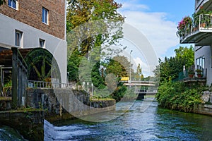 River in the city among buildings. On the left bank is a wheel of an old water mill