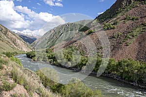 River flowing between green hills with snow-capped mountain peaks on the horizon against a cloudy sky