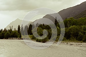 River flowing through a mountain valley landscape with misty clouds over the mountain peaks