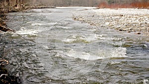 River flowing in spring, water forming white waves, round stones on shore, slow motion video