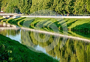 The river flows through the city. On the calm surface of the river banks are reflected. Slovak river Nitra on a bright sunny day