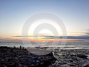 The river flows into the sea on a rocky beach against the backdrop of a sunset