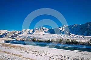 River flows through a snow-covered valley. Winter landscape of mountain peaks and blue sky. Fantastic panorama of wildlife, space