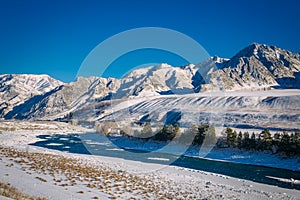 River flows through a snow-covered valley. Winter landscape of mountain peaks and blue sky. Fantastic panorama of wildlife, space