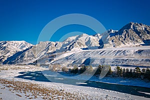 River flows through a snow-covered valley. Winter landscape of mountain peaks and blue sky. Fantastic panorama of wildlife, space