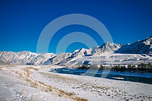 River flows through a snow-covered valley. Winter landscape of mountain peaks and blue sky. Fantastic panorama of wildlife, space