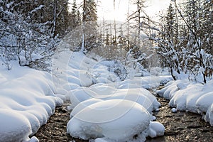 River flows at sunset in winter in drifts in forest