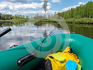 The river from a green fisherman`s rubber boat, calm river water with reflections and bright green vegetation on the shore