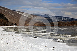 A river with ice floes against the backdrop of mountains in the snow and cloudy sky.