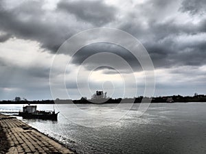 River landscape with a lonely ship at anchor. Cloudy weather with heavy clouds. Reflection of clouds in the water. The opposite