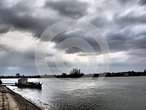 River landscape with a lonely ship at anchor. Cloudy weather with heavy clouds. Reflection of clouds in the water. The opposite