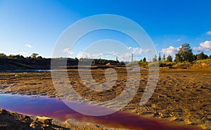 River with polluted red toxic water and soil and with garbage on the shore. environmental pollution by factory