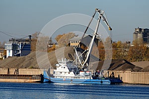 River port. Cargo barges, tug and port crane on the river bank, river sand mining.