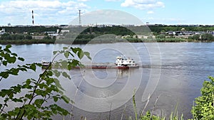 A river push boat carries a barge loaded with sand on the river in summer.